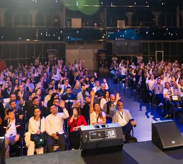 Asistentes con las manos arriba en un auditorio iluminado en azul